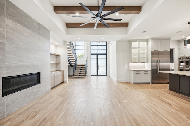 kitchen with ceiling fan, stainless steel appliances, beam ceiling, a tiled fireplace, and light hardwood / wood-style floors