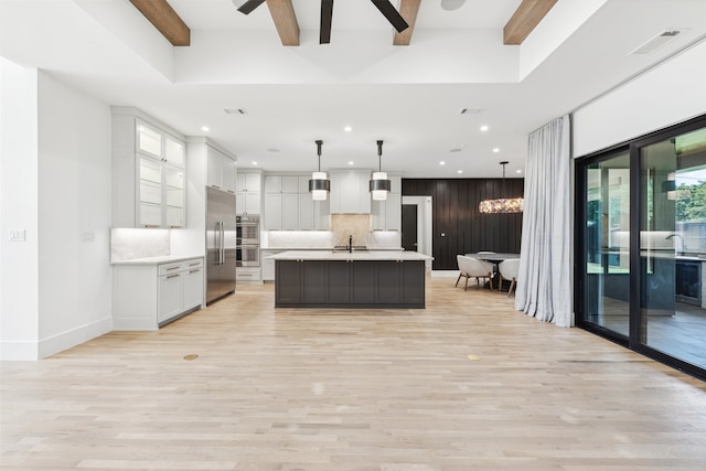 kitchen with white cabinets, decorative light fixtures, beamed ceiling, and a center island with sink