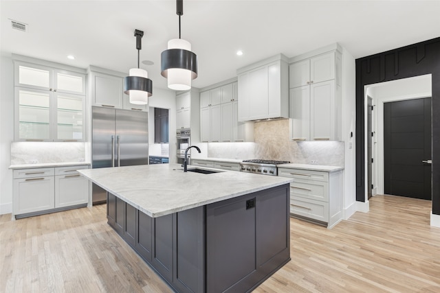 kitchen featuring decorative light fixtures, tasteful backsplash, sink, a center island with sink, and light wood-type flooring