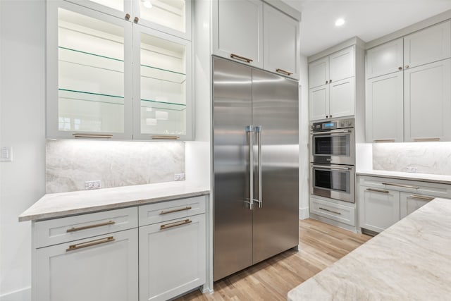 kitchen with light stone countertops, appliances with stainless steel finishes, backsplash, and light hardwood / wood-style floors