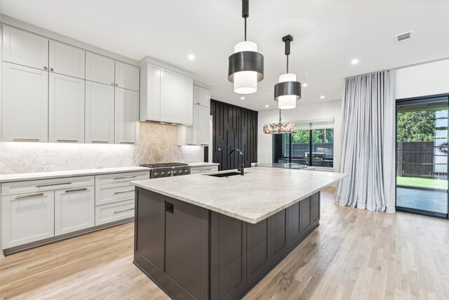 kitchen with sink, white cabinetry, hanging light fixtures, light stone countertops, and a large island with sink