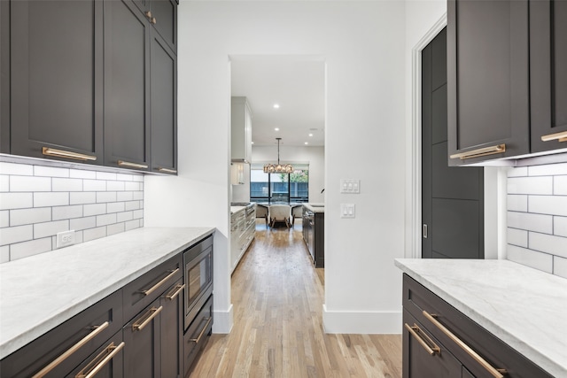 kitchen featuring pendant lighting, light hardwood / wood-style flooring, stainless steel microwave, tasteful backsplash, and light stone countertops