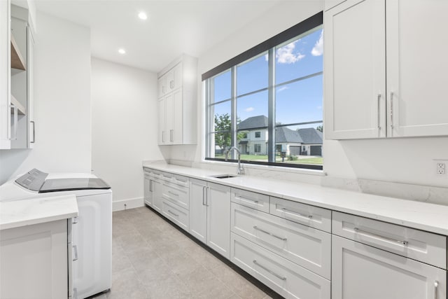 kitchen with washing machine and clothes dryer, sink, white cabinets, and light stone counters