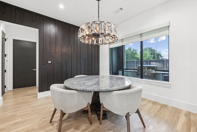 dining area with light hardwood / wood-style floors, a chandelier, and wood walls