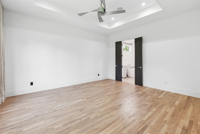 spare room with a raised ceiling, ceiling fan, and light wood-type flooring