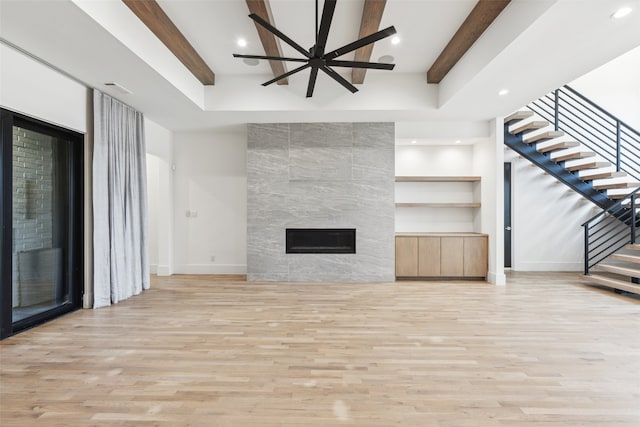 unfurnished living room with beamed ceiling, a tile fireplace, ceiling fan, and light hardwood / wood-style floors