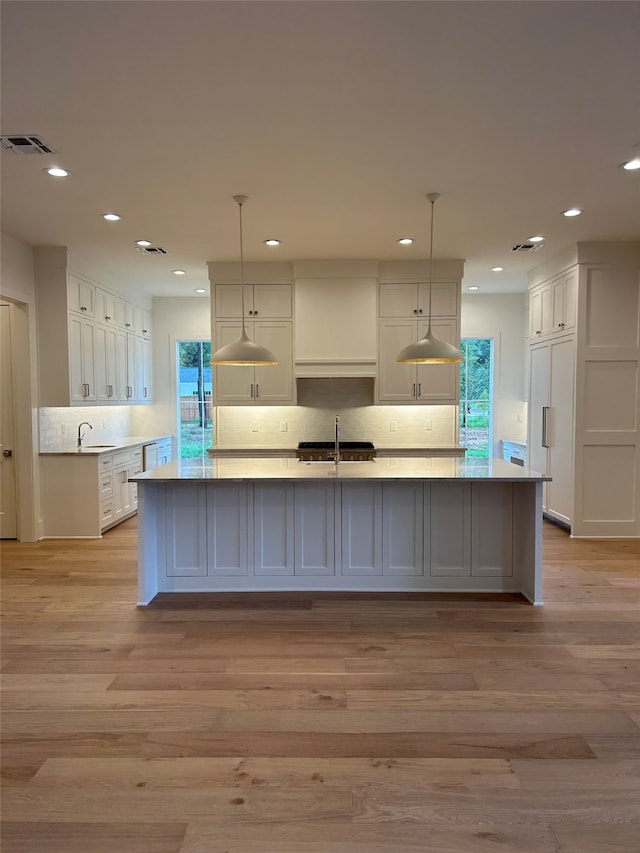 kitchen with light hardwood / wood-style flooring, white cabinetry, hanging light fixtures, and a kitchen island with sink