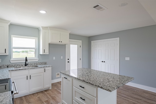 kitchen featuring white cabinets, light hardwood / wood-style floors, light stone counters, and sink