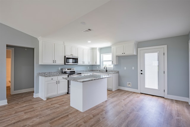 kitchen featuring light stone countertops, stainless steel appliances, white cabinets, a kitchen island, and light wood-type flooring