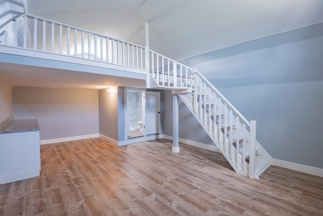 stairs with hardwood / wood-style floors and high vaulted ceiling