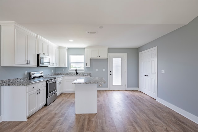 kitchen with a center island, light stone counters, appliances with stainless steel finishes, white cabinets, and light wood-type flooring