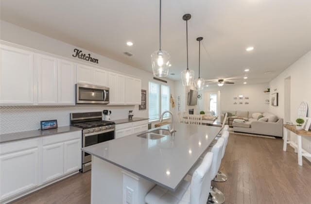 kitchen with dark wood-type flooring, sink, a kitchen island with sink, and stainless steel appliances