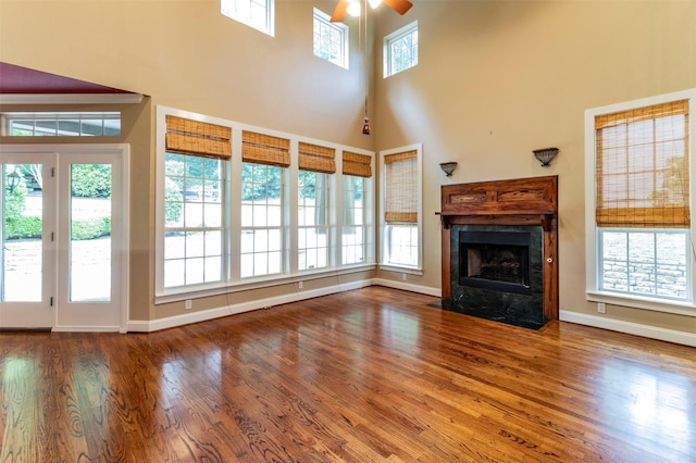 unfurnished living room with a high end fireplace, a high ceiling, hardwood / wood-style flooring, and ceiling fan