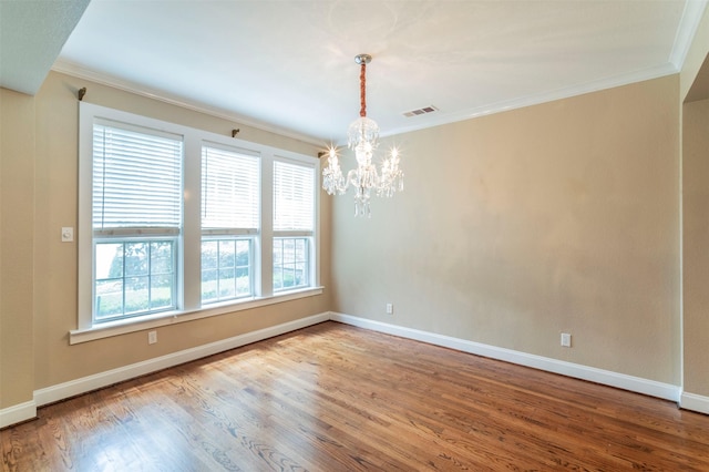 empty room with ornamental molding, hardwood / wood-style floors, a healthy amount of sunlight, and an inviting chandelier