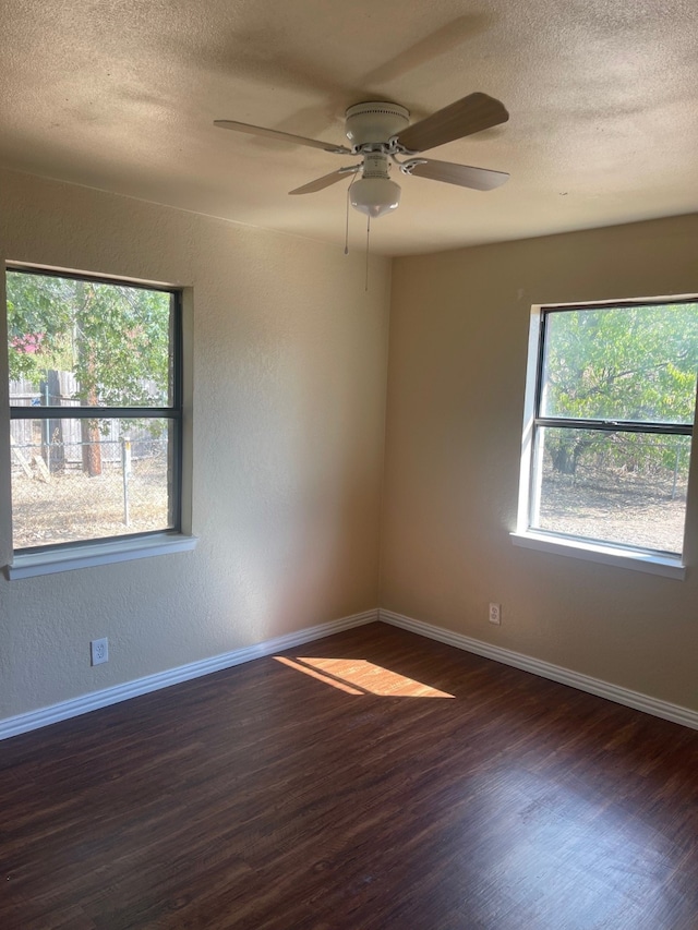 spare room with a wealth of natural light, ceiling fan, dark wood-type flooring, and a textured ceiling