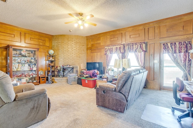 carpeted living room featuring wood walls, a brick fireplace, brick wall, ceiling fan, and a textured ceiling