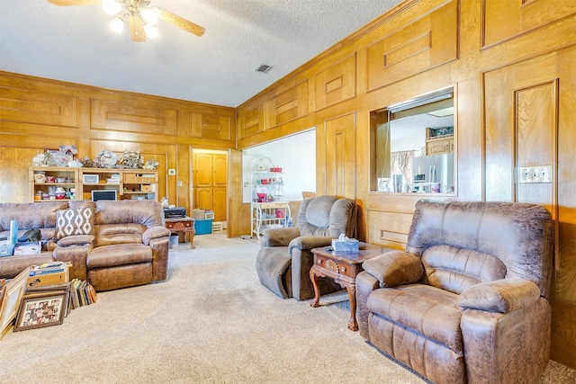 living room with a textured ceiling, ceiling fan, light carpet, and wooden walls