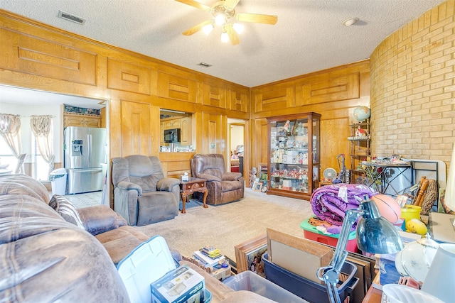 carpeted living room featuring a textured ceiling, wood walls, and ceiling fan