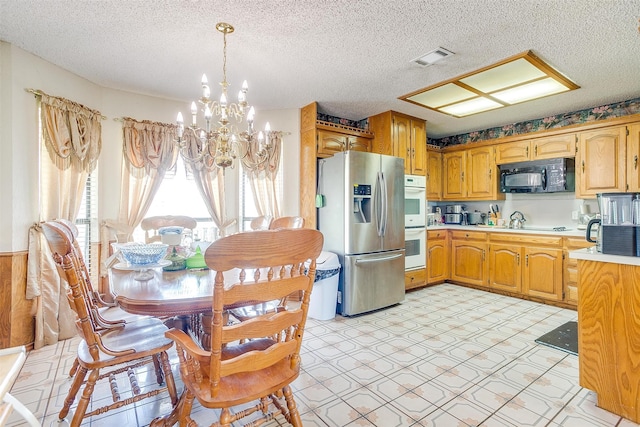 kitchen featuring white double oven, light tile floors, stainless steel fridge, pendant lighting, and an inviting chandelier