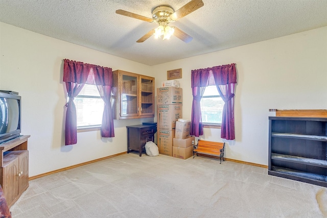 living area featuring light colored carpet, ceiling fan, and a textured ceiling