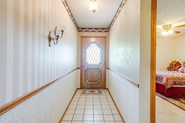 doorway with a textured ceiling, ceiling fan, and light tile flooring