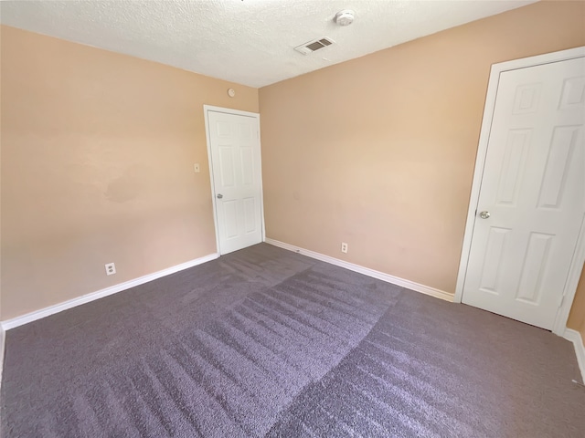 unfurnished room featuring dark colored carpet and a textured ceiling