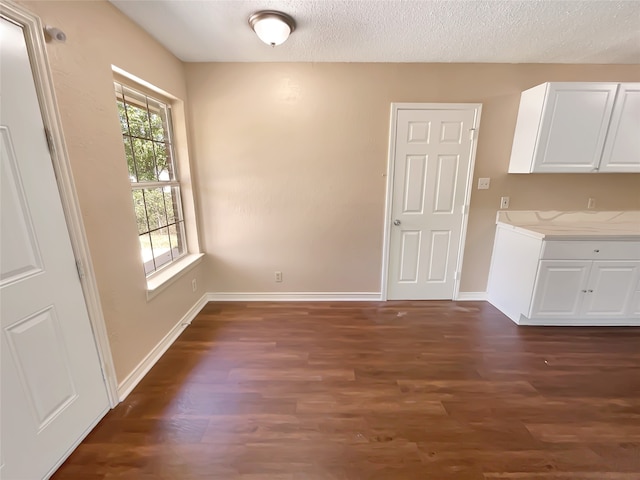 unfurnished dining area with a textured ceiling and dark wood-type flooring