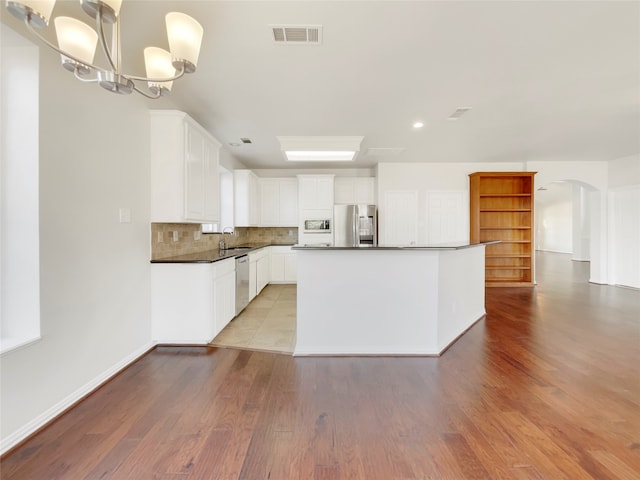 kitchen featuring light wood-type flooring, decorative backsplash, white cabinets, appliances with stainless steel finishes, and decorative light fixtures