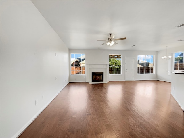 unfurnished living room with wood-type flooring, ceiling fan with notable chandelier, and a healthy amount of sunlight