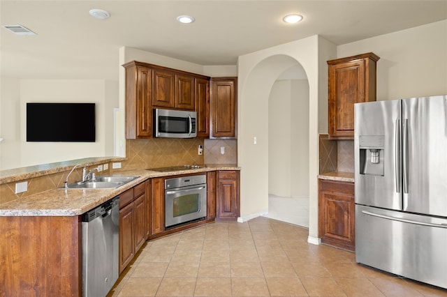 kitchen featuring light stone counters, backsplash, light tile floors, sink, and appliances with stainless steel finishes