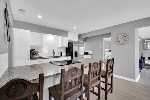 kitchen featuring light wood-type flooring, sink, a breakfast bar area, stainless steel fridge, and ceiling fan