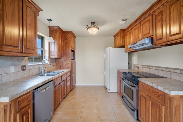 kitchen featuring sink, backsplash, hanging light fixtures, stainless steel appliances, and tile countertops