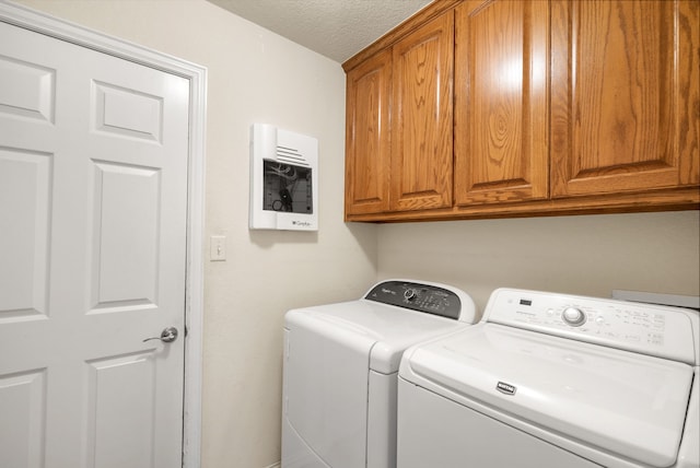 clothes washing area featuring washer and dryer, cabinets, and a textured ceiling