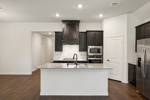 kitchen featuring sink, dark hardwood / wood-style flooring, appliances with stainless steel finishes, a kitchen island with sink, and premium range hood