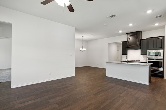 kitchen featuring backsplash, dark wood-type flooring, an island with sink, custom exhaust hood, and appliances with stainless steel finishes