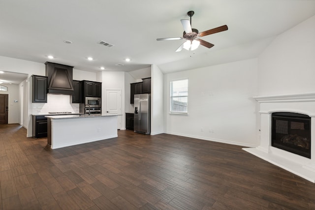 kitchen with appliances with stainless steel finishes, custom range hood, dark hardwood / wood-style flooring, and a center island with sink