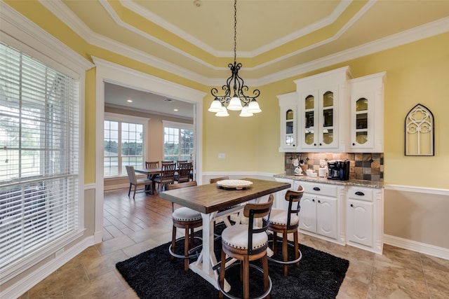 dining space with a notable chandelier, ornamental molding, light tile floors, and a raised ceiling