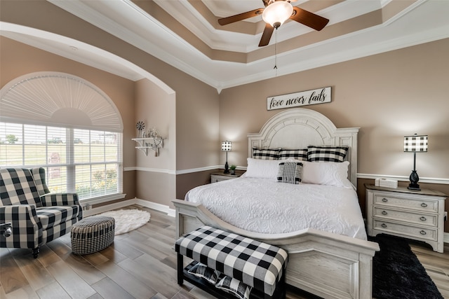 bedroom with a tray ceiling, hardwood / wood-style flooring, ornamental molding, and ceiling fan