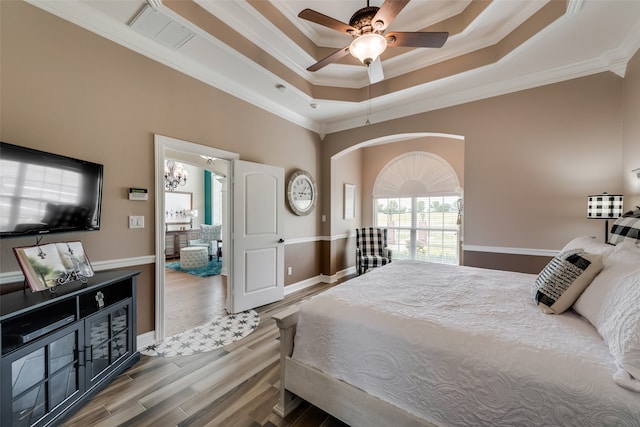 bedroom with ornamental molding, wood-type flooring, ceiling fan, and a raised ceiling