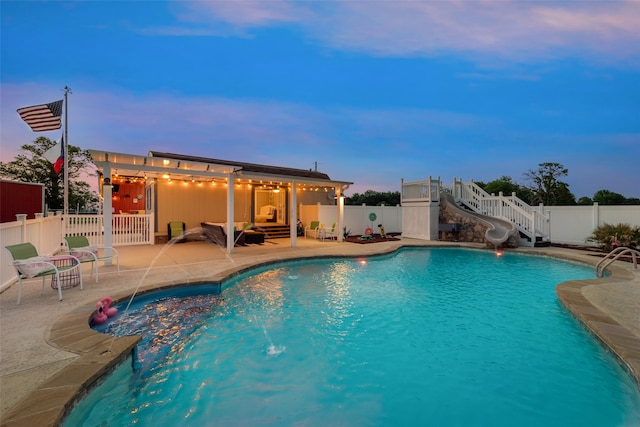 pool at dusk featuring a water slide, pool water feature, and a patio