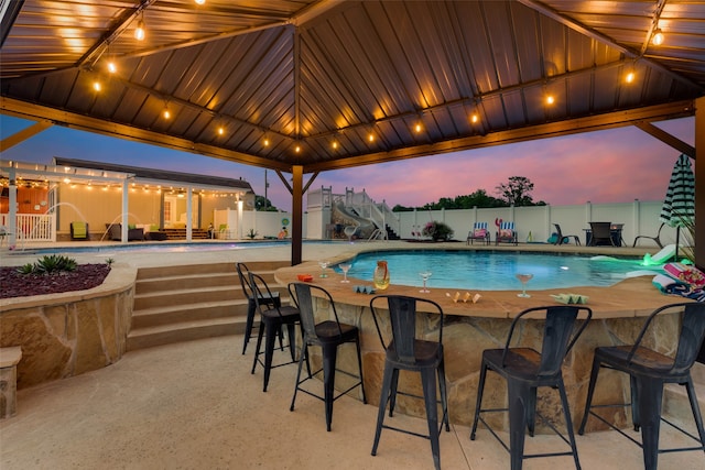 pool at dusk featuring a patio area and an outdoor bar