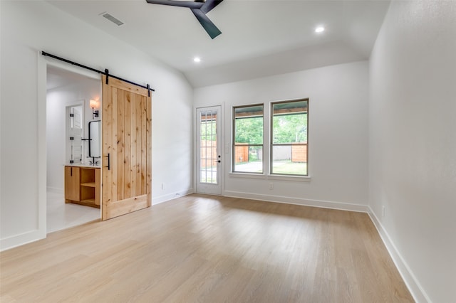 unfurnished room with lofted ceiling, light hardwood / wood-style floors, and a barn door