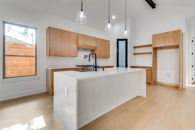 kitchen featuring pendant lighting, beamed ceiling, tasteful backsplash, light hardwood / wood-style floors, and an island with sink