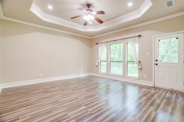 unfurnished room with plenty of natural light, a raised ceiling, light wood-type flooring, and ornamental molding