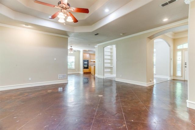 unfurnished living room with crown molding, ceiling fan, dark tile patterned floors, built in features, and a tray ceiling