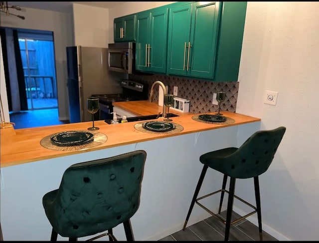 kitchen featuring appliances with stainless steel finishes, tasteful backsplash, green cabinetry, and wood counters