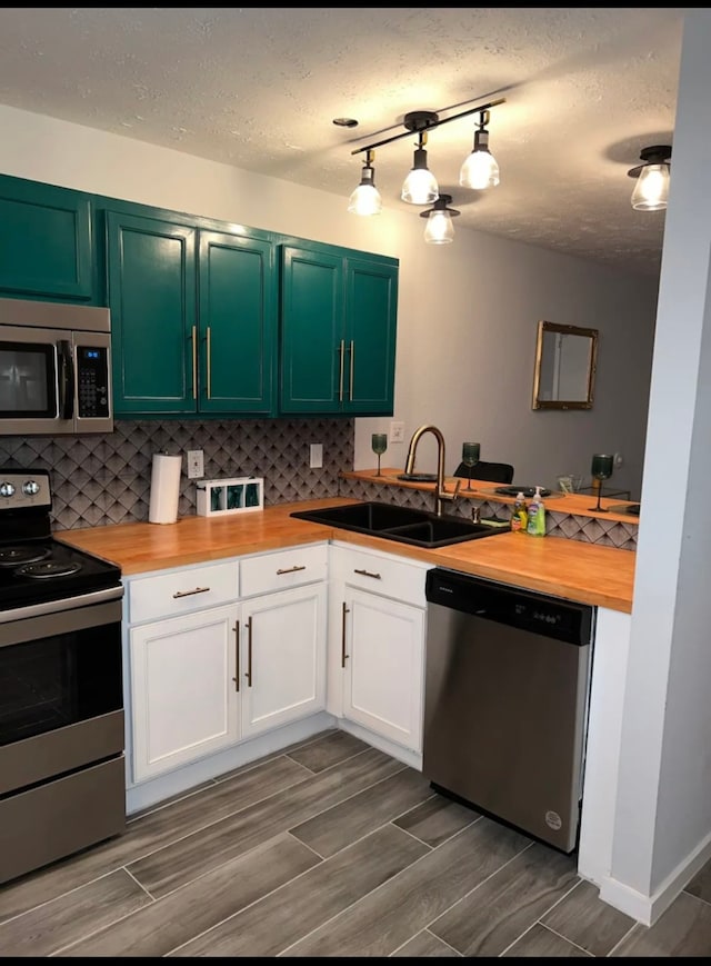 kitchen with white cabinetry, backsplash, rail lighting, appliances with stainless steel finishes, and sink