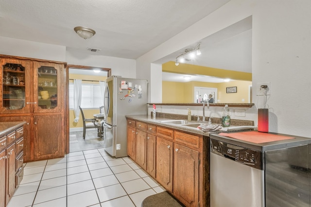 kitchen with rail lighting, appliances with stainless steel finishes, light tile floors, sink, and a textured ceiling