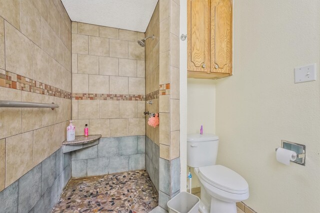 bathroom with toilet, a textured ceiling, and a tile shower