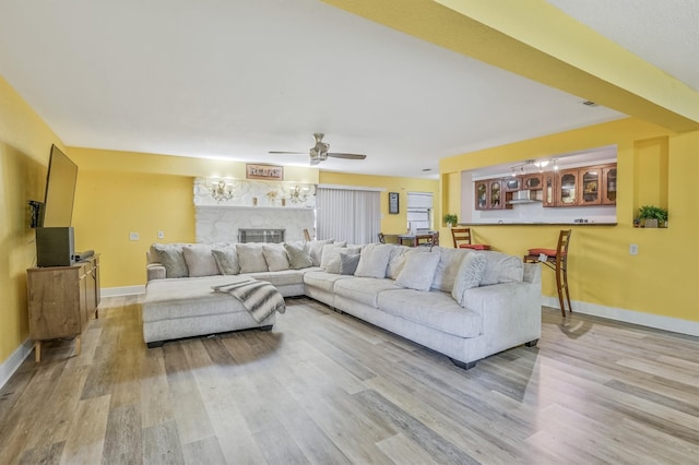 living room featuring ceiling fan, hardwood / wood-style flooring, and a stone fireplace